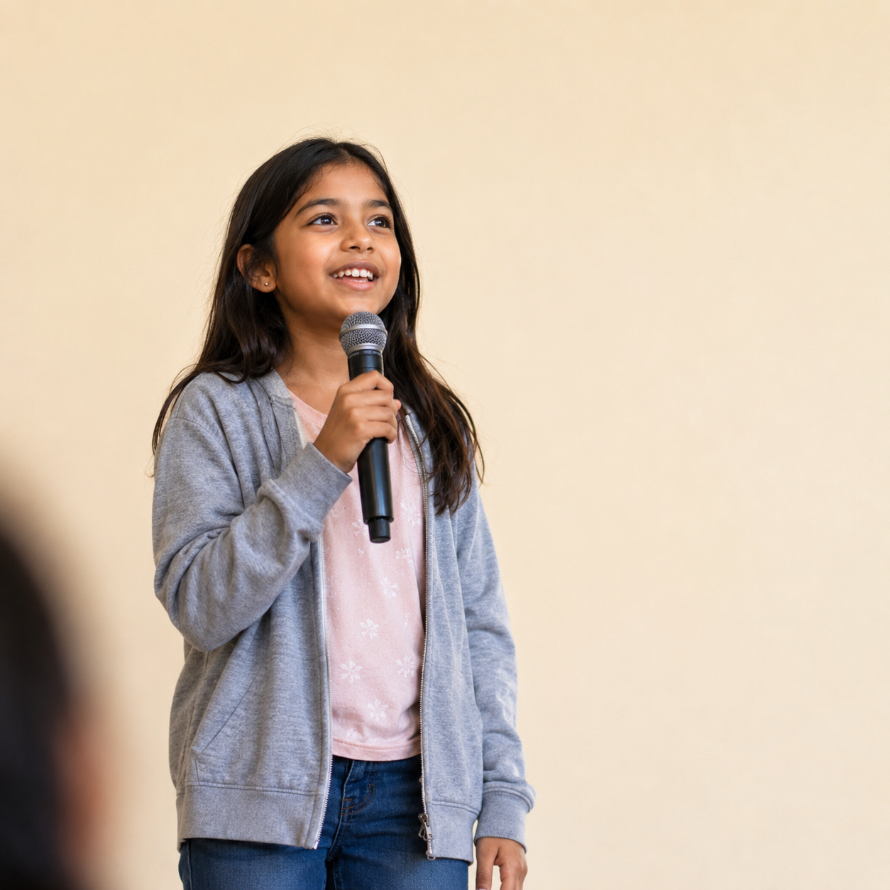 A girl smiling and speaking into a microphone, looking up with confidence